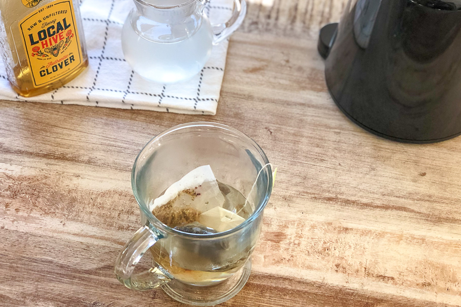 Mug with water and tea bags with honey and lemonade in the background
