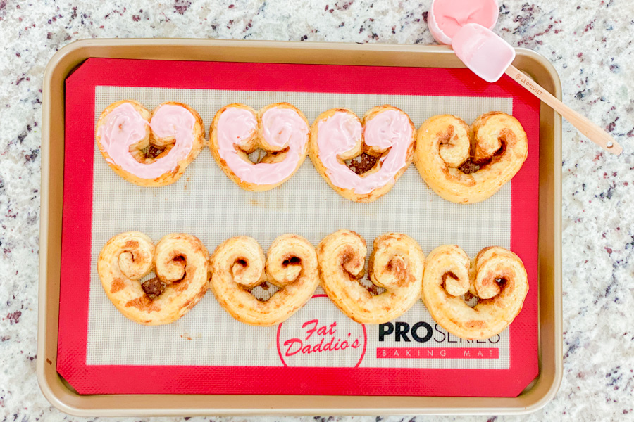 Cooked heart shaped cinnamon rolls with icing being applied 