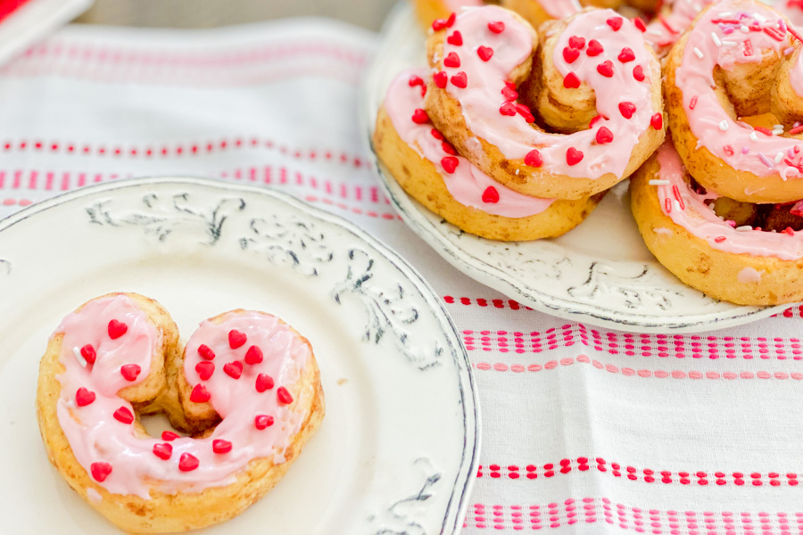 Cinnamon Roll shaped like a heart with pink icing on a plate