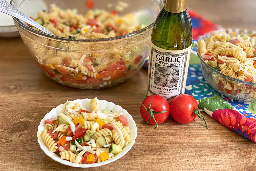Pepperoni Pasta Salad in a bowl with larger batch in background with tomatoes and salad dressing
