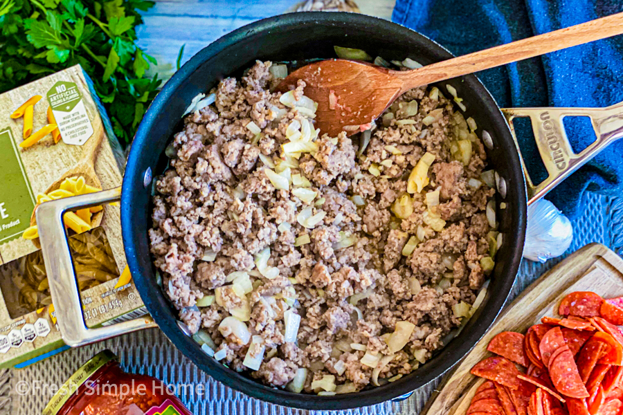 Ground sausage and diced onion being browned in a skillet. 
