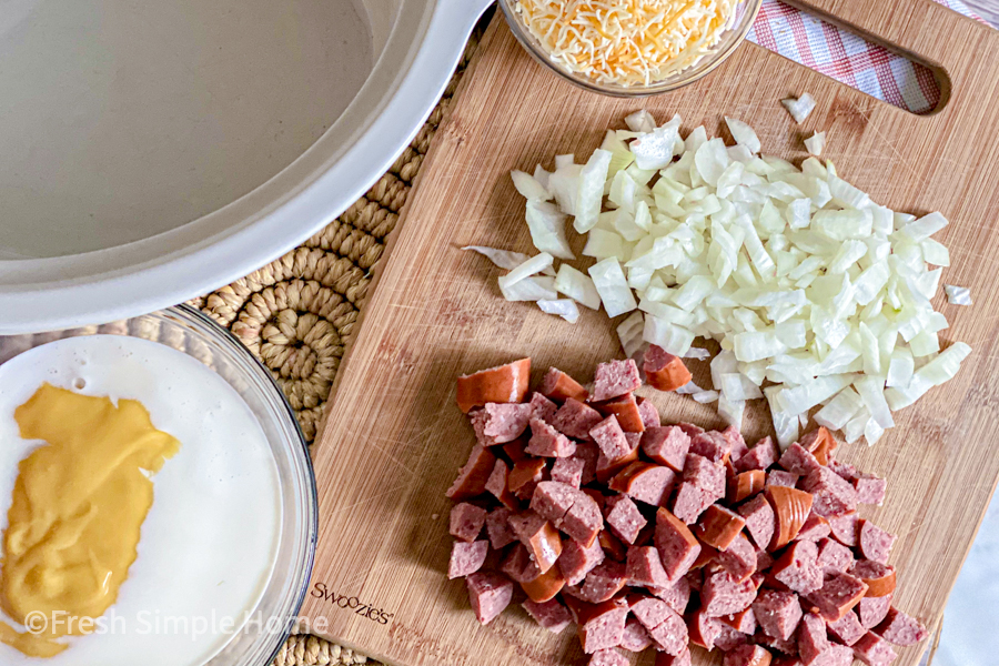 A cutting board with diced kielbasa, onions, and shredded cheese, all before being put in a crockpot. 