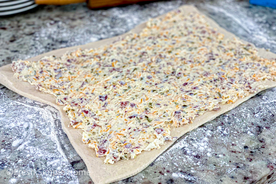 The pizza dough laid out on a flour-dusted counter with the cream cheese mixture spread on top of it. 