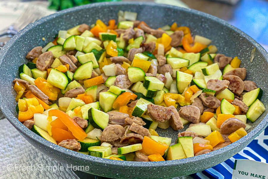A gray skillet with diced chicken sausage, bell peppers, onions, and zucchini. 