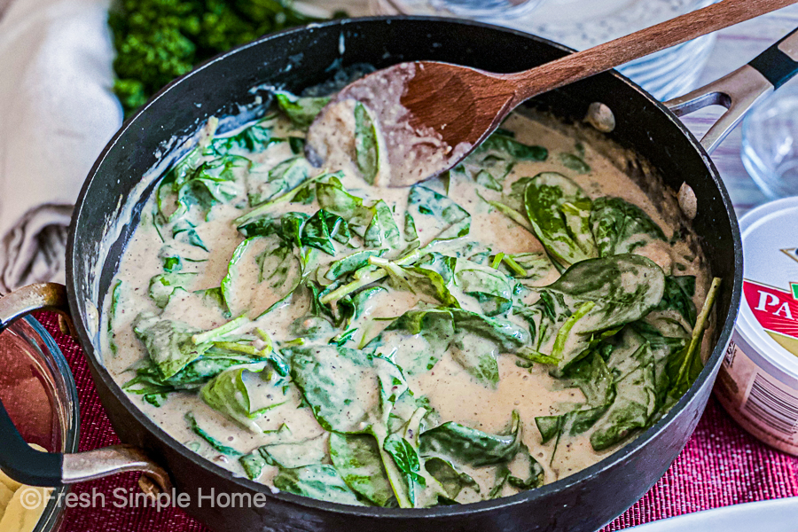 A black skillet with creamy sauce and wilting spinach being stirred together. 