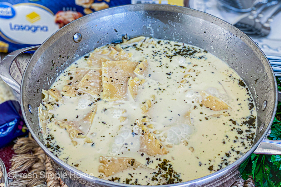 The stainless steel skillet with the milk mixture and broken lasagna noodles being boiled. 