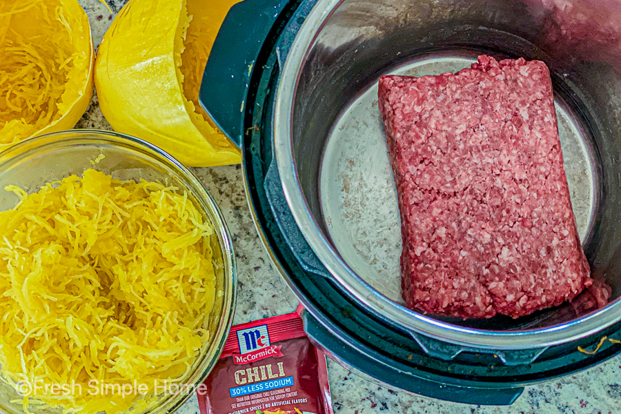 Uncooked ground beef in the instant pot next to a bowl of cooked spaghetti squash. 